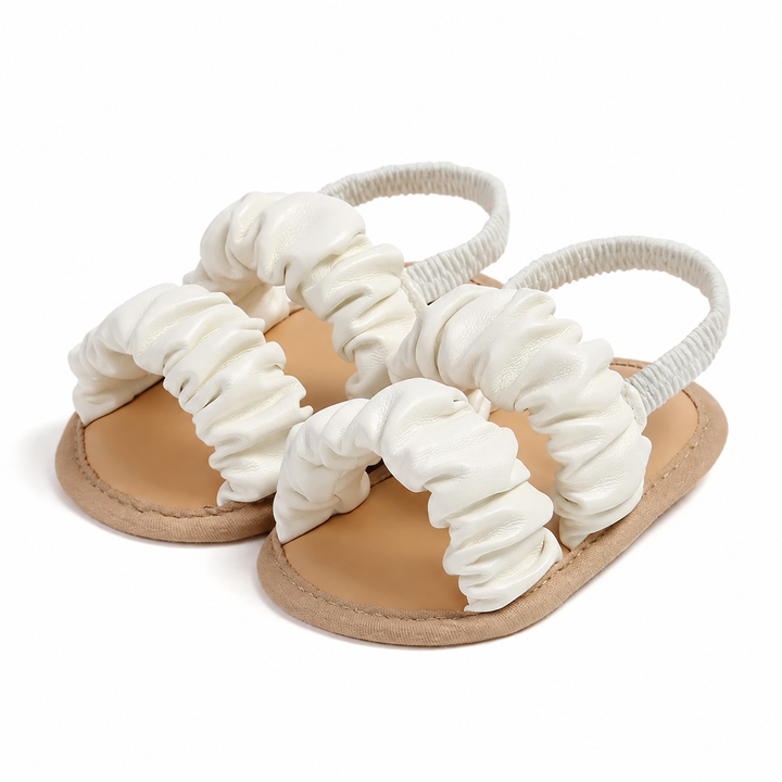 White baby girl sandals with gathered straps, tan soles, and elastic heel straps