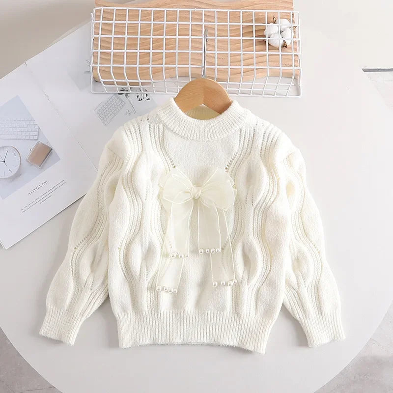 White girls' cable-knit sweater with a sheer bow, pearl-look accents, and ribbed trim