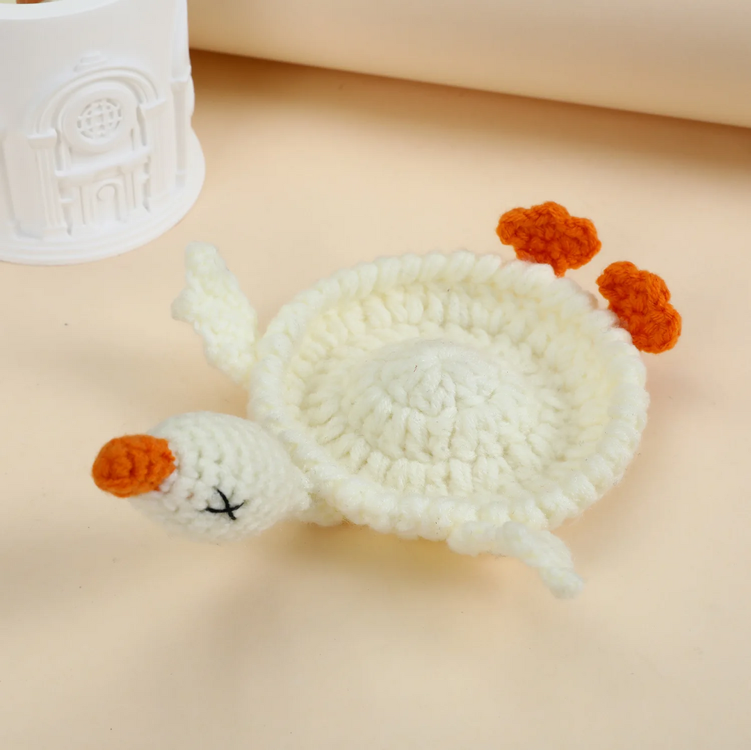 White crocheted goose coaster with an orange bill and feet