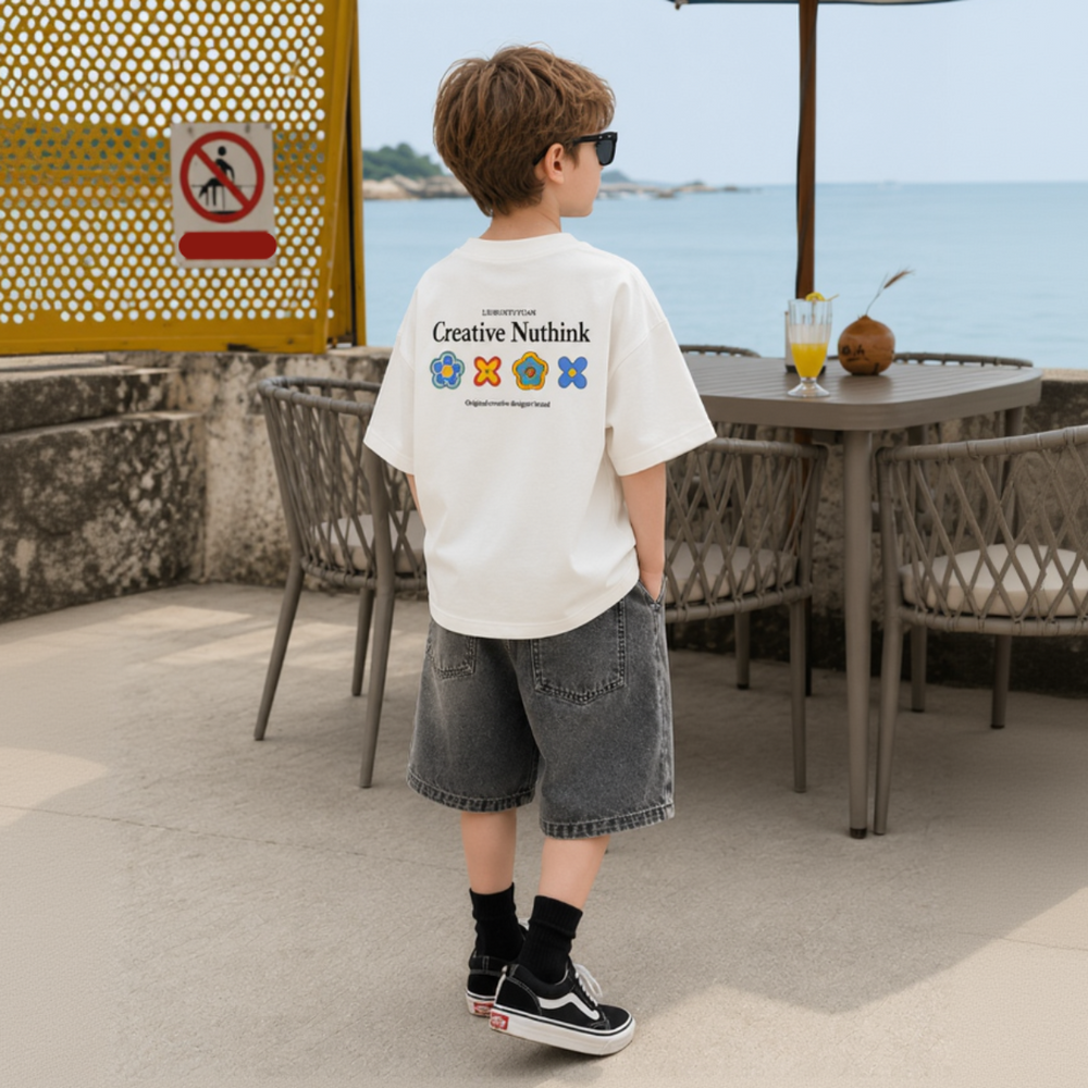 Boy wearing a white graphic T-shirt and denim shorts beside a seaside patio