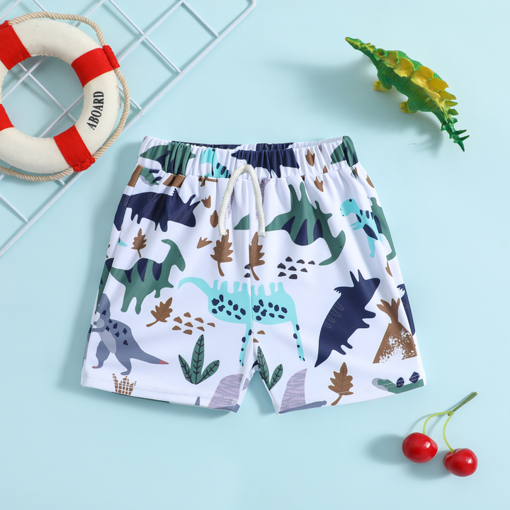 White swim trunks with green, navy, and brown dinosaur prints and a white drawstring
