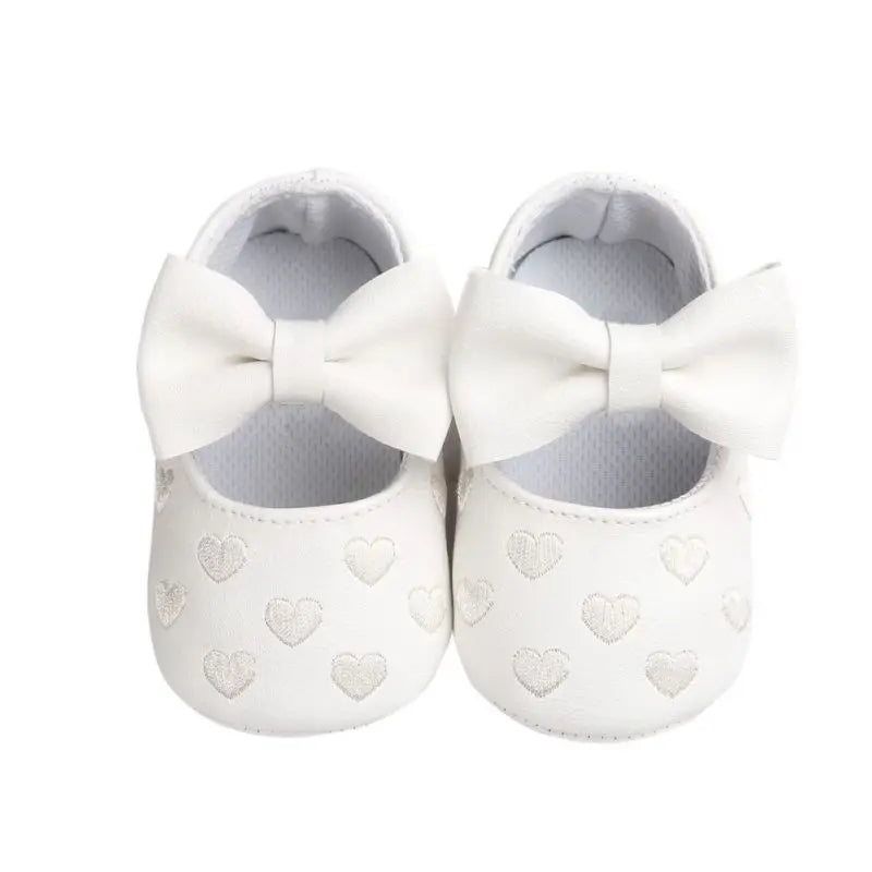 White baby shoes with matching bows and heart details across the toes