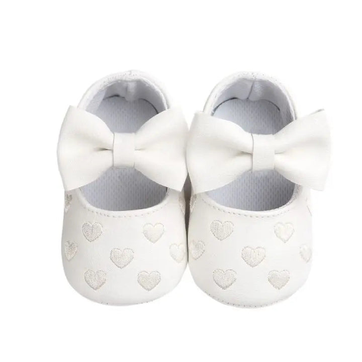 White baby shoes with matching bows and heart details across the toes