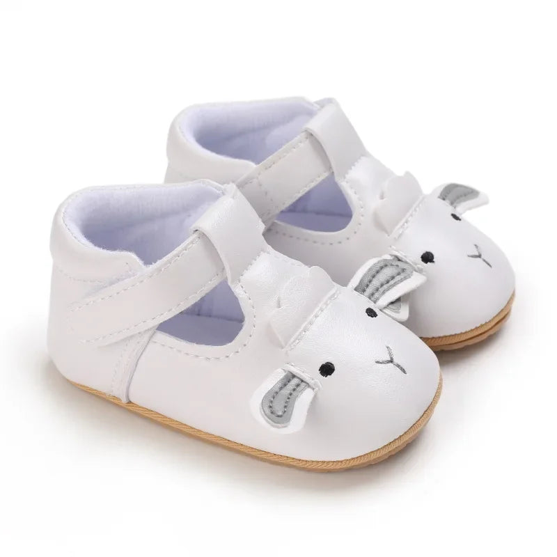 White lamb baby shoes shown from the side with straps and tan soles