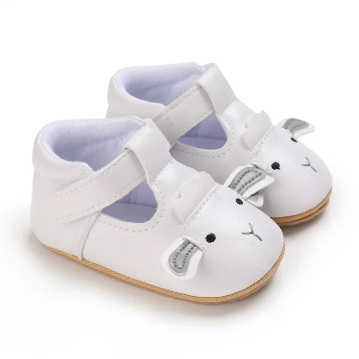 White lamb baby shoes shown from the side with straps and tan soles