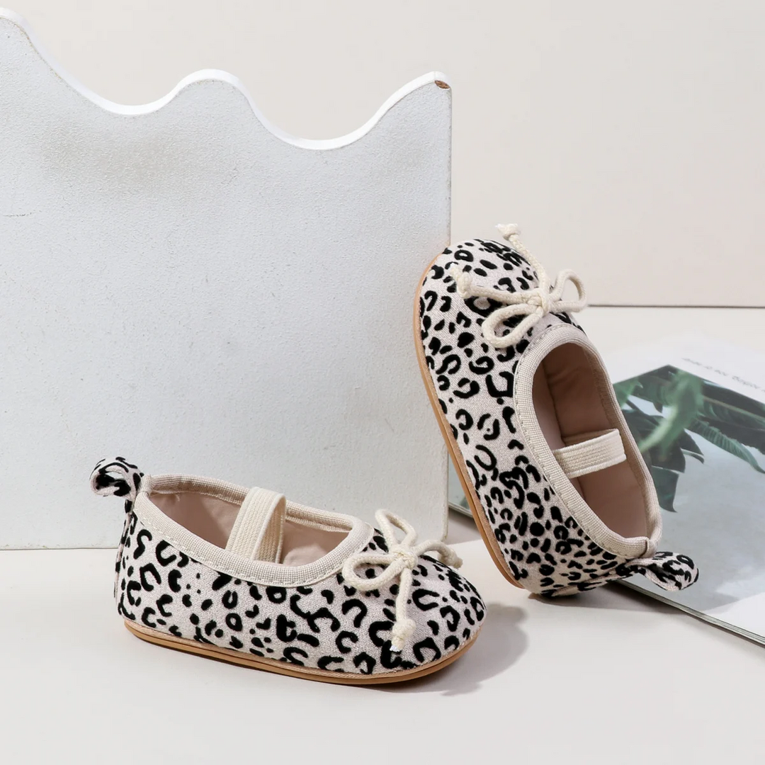 White leopard-print baby shoes shown from the side and above with elastic straps and bows