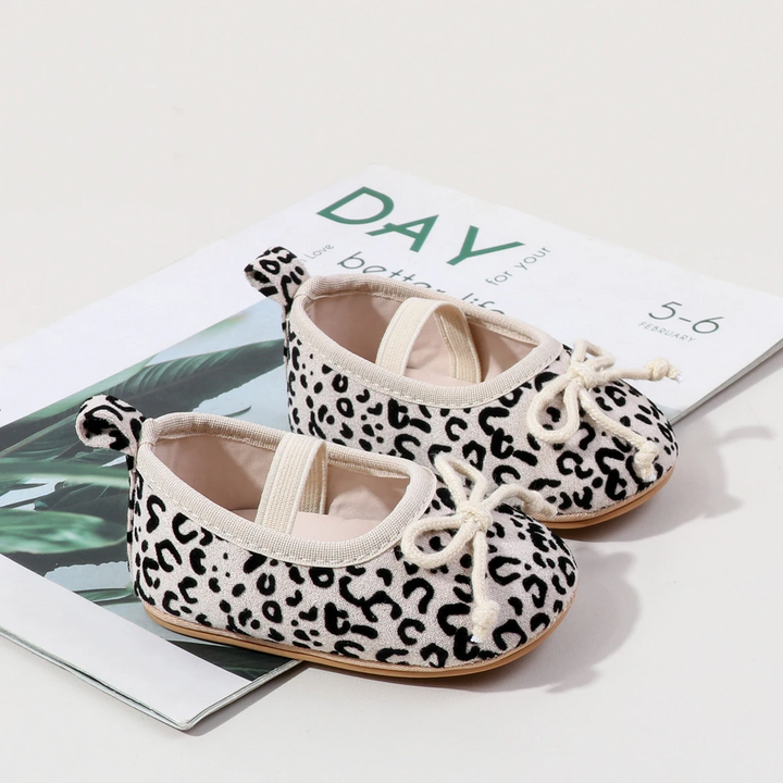 Pair of white leopard-print baby shoes with cream elastic straps and toe bows