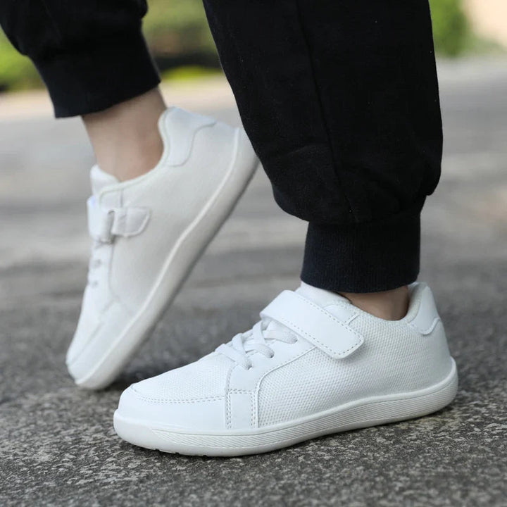 Side view of white low-top sneakers worn outdoors with black pants