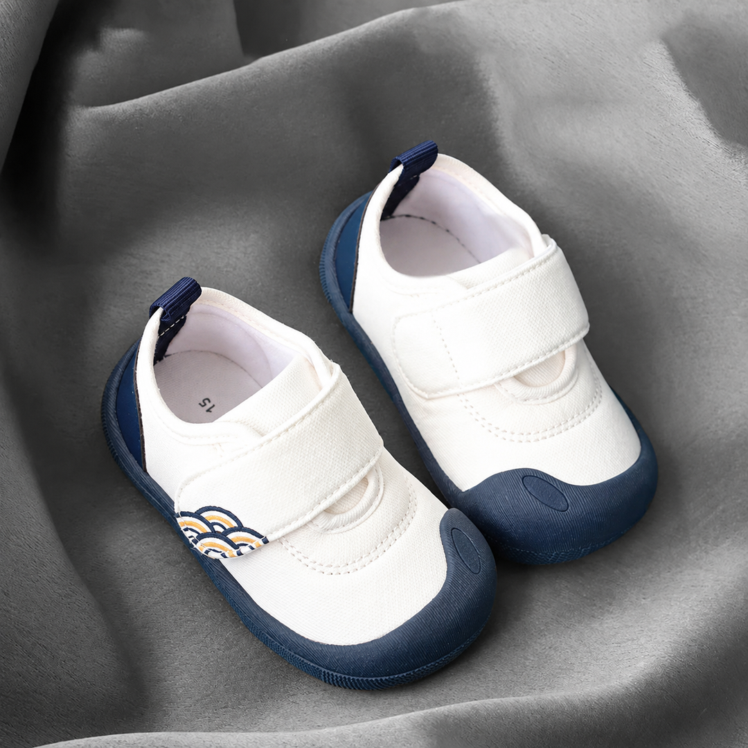 Pair of white baby sneakers with navy toe caps, navy soles, and wide strap closures