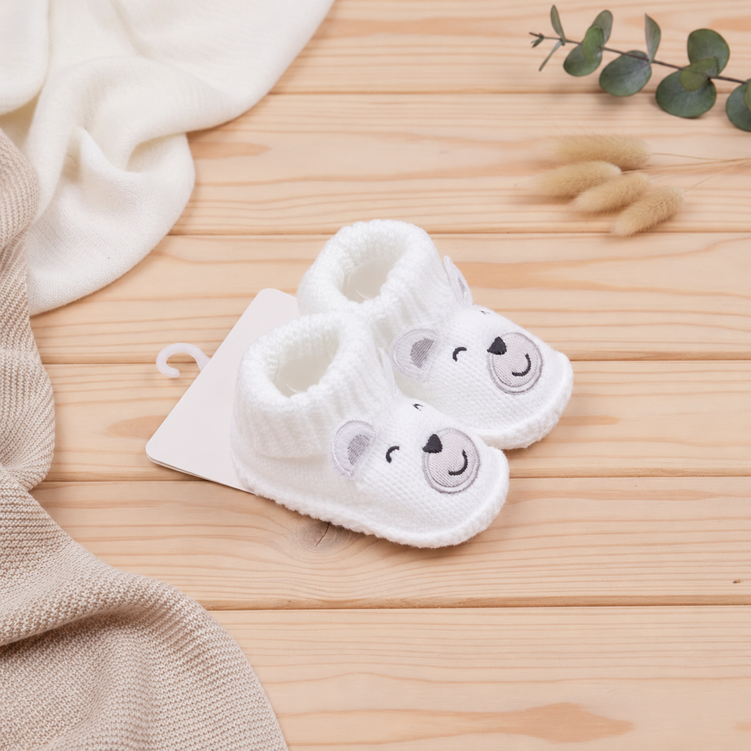 White polar bear baby booties shown at an angle on a wooden surface