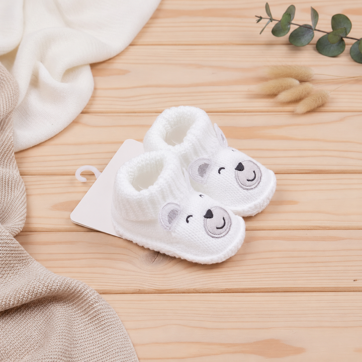 White polar bear baby booties shown at an angle on a wooden surface