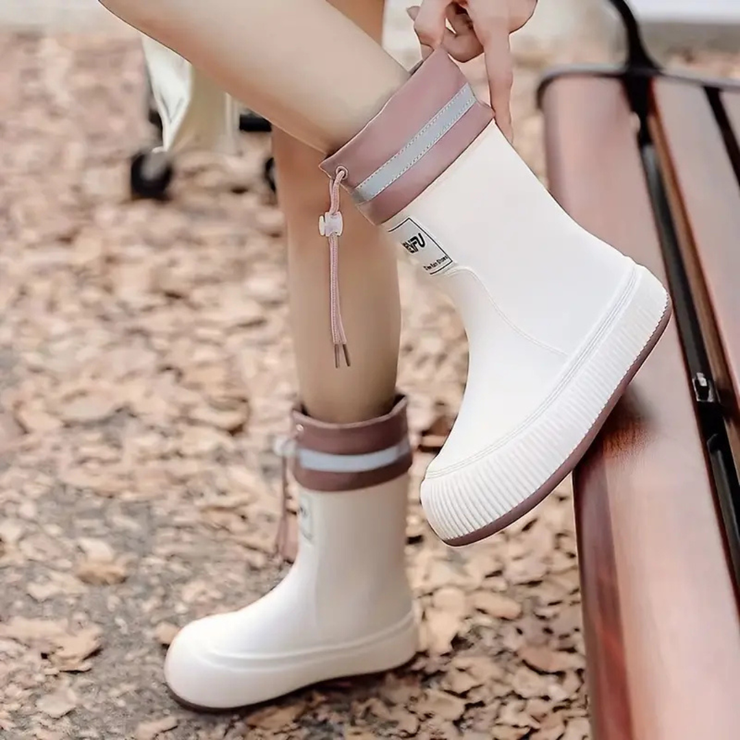A hand pulling on the pink cuff of a white rain boot beside an outdoor bench