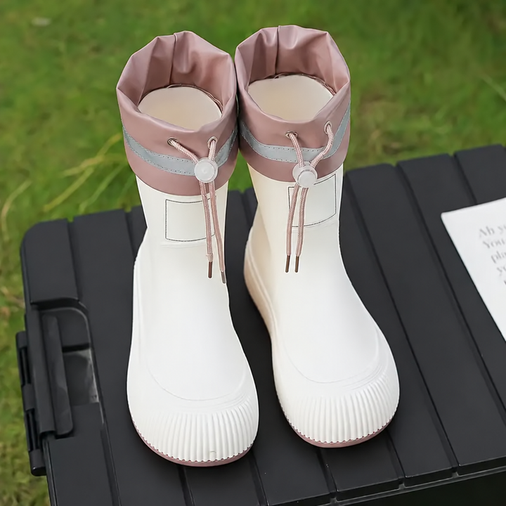 White rain boots with pink drawstring cuffs viewed from the front on an outdoor table