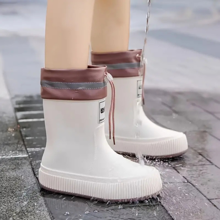 White rain boots with pink cuffs under running water on pavement