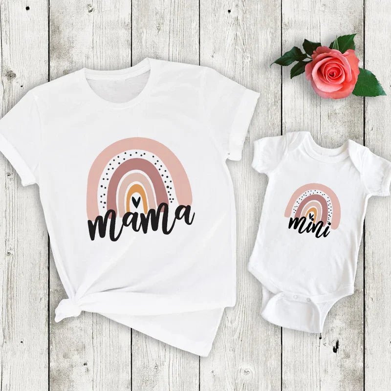 White mama T-shirt and mini baby bodysuit with pink rainbow prints on a wood background