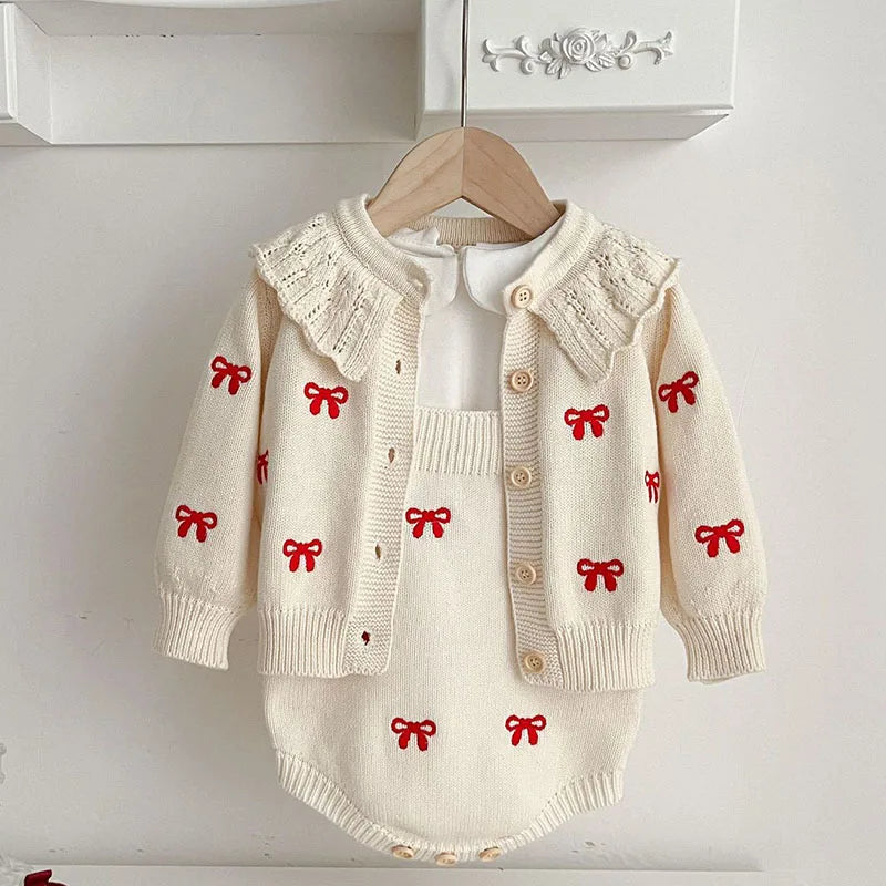 White knit cardigan and bodysuit with red bow motifs hanging over a collared shirt