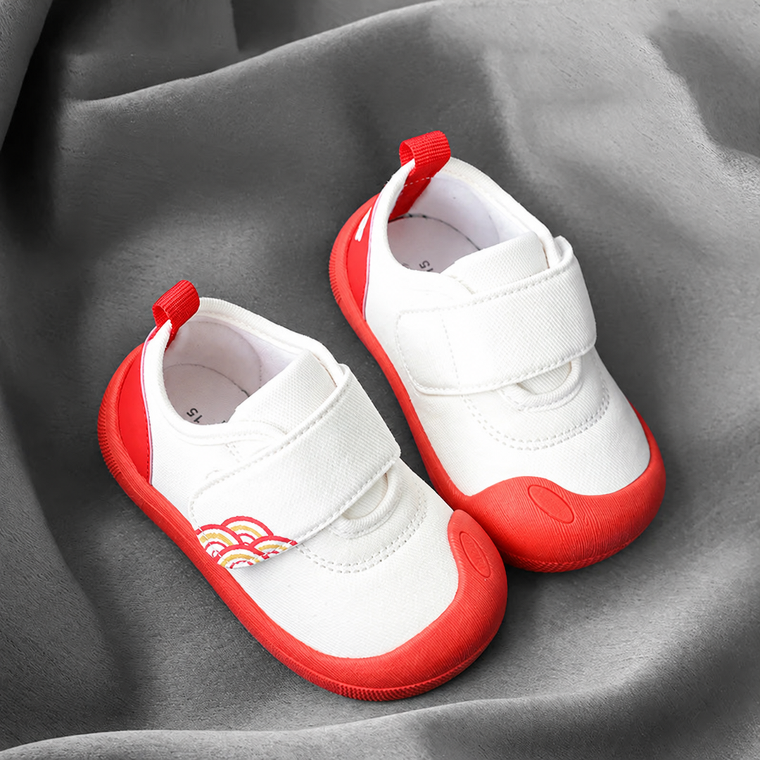 Pair of white baby sneakers with red toe caps, red soles, and wide strap closures