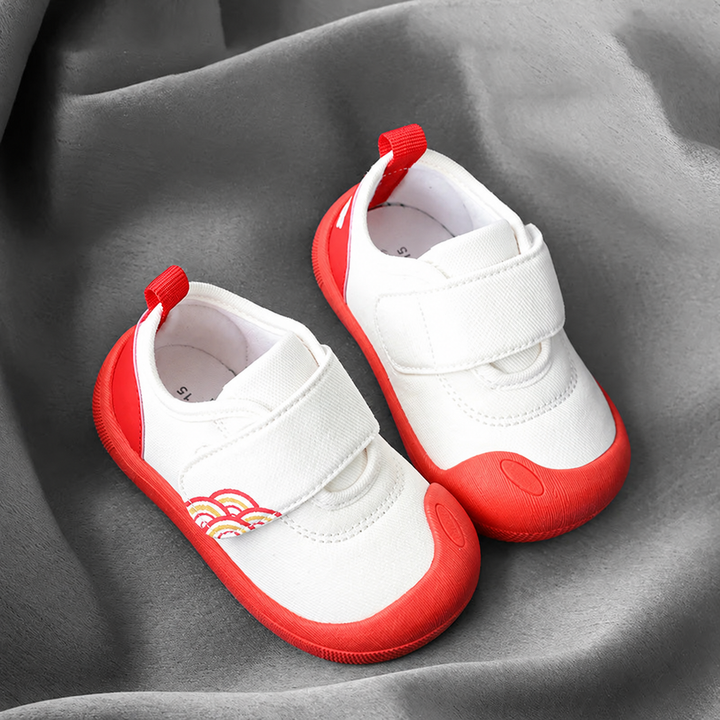 Pair of white baby sneakers with red toe caps, red soles, and wide strap closures