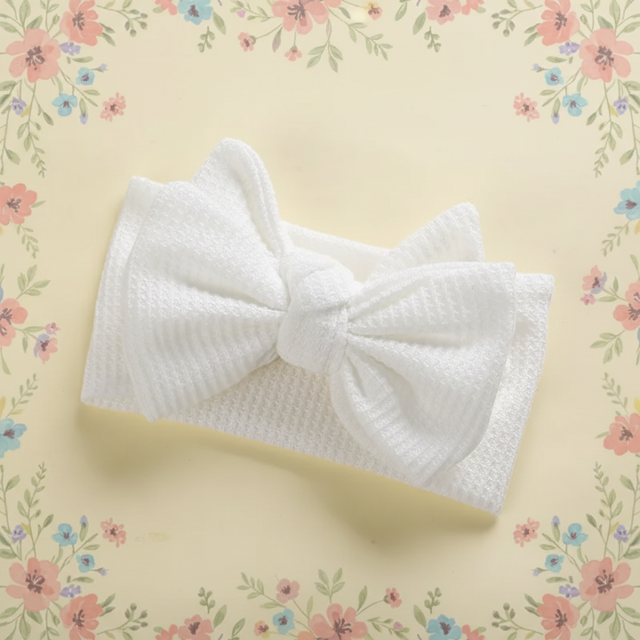 White ribbed baby headband with a large bow on a floral background
