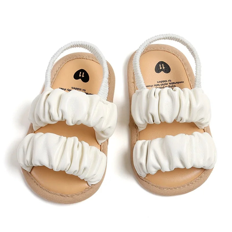 White baby sandals with two ruched front straps and elastic heel straps, viewed from above