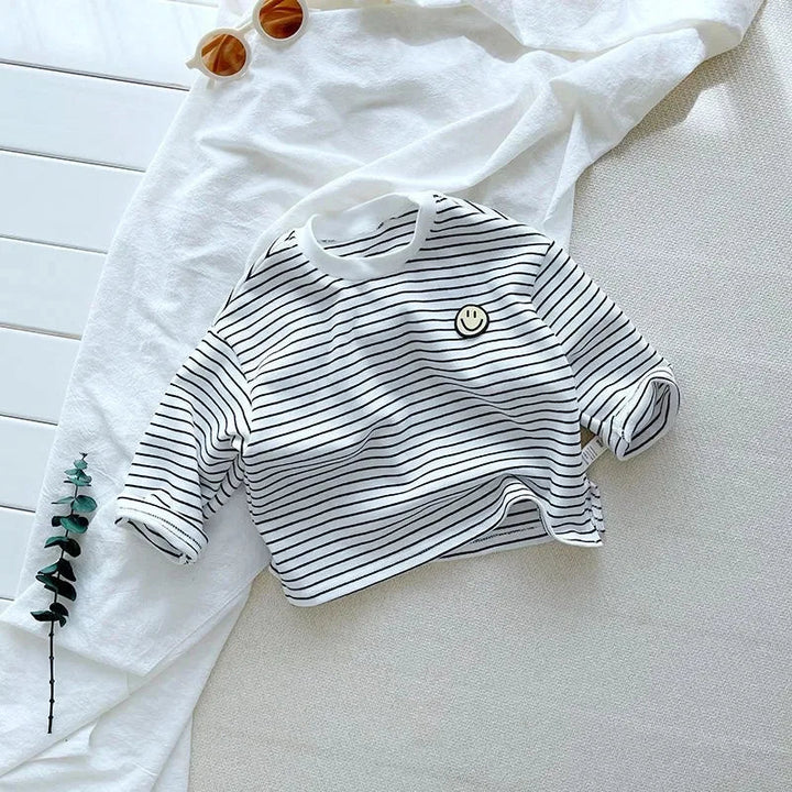 White long-sleeve shirt with thin black stripes and a smile patch, displayed with rolled cuffs.