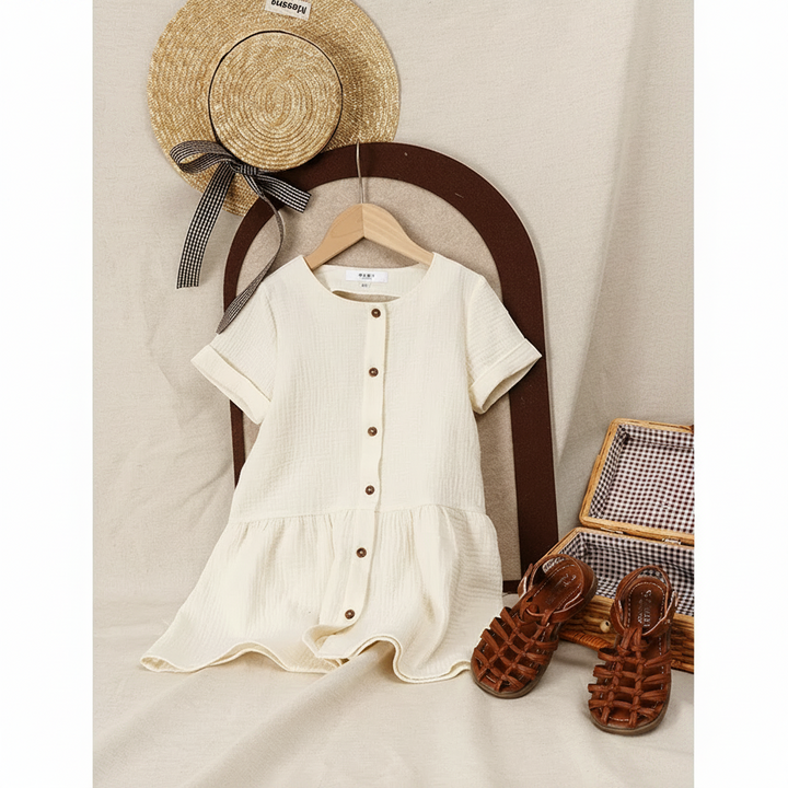 White button-front dress hanging below a straw hat, with brown sandals beside it.