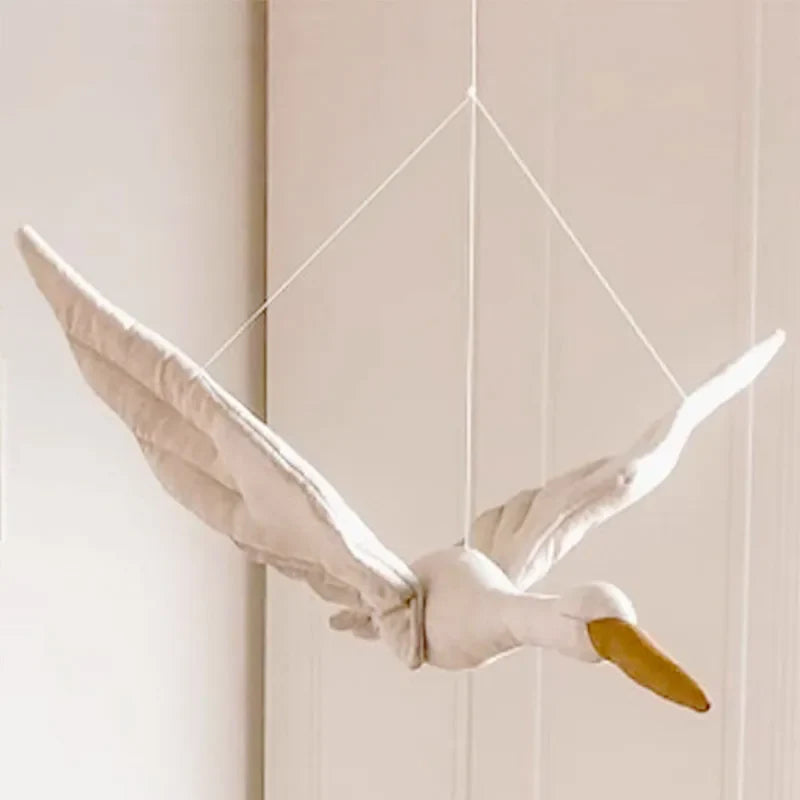 White fabric swan decoration hanging by cords with raised wings and a yellow beak