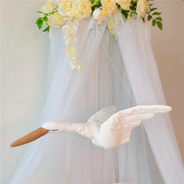 White swan decoration with spread wings hanging in front of a sheer canopy
