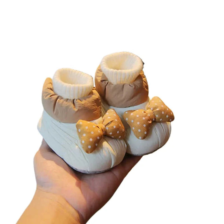 White and tan baby shoes with dotted bows and cream ribbed cuffs against a white background