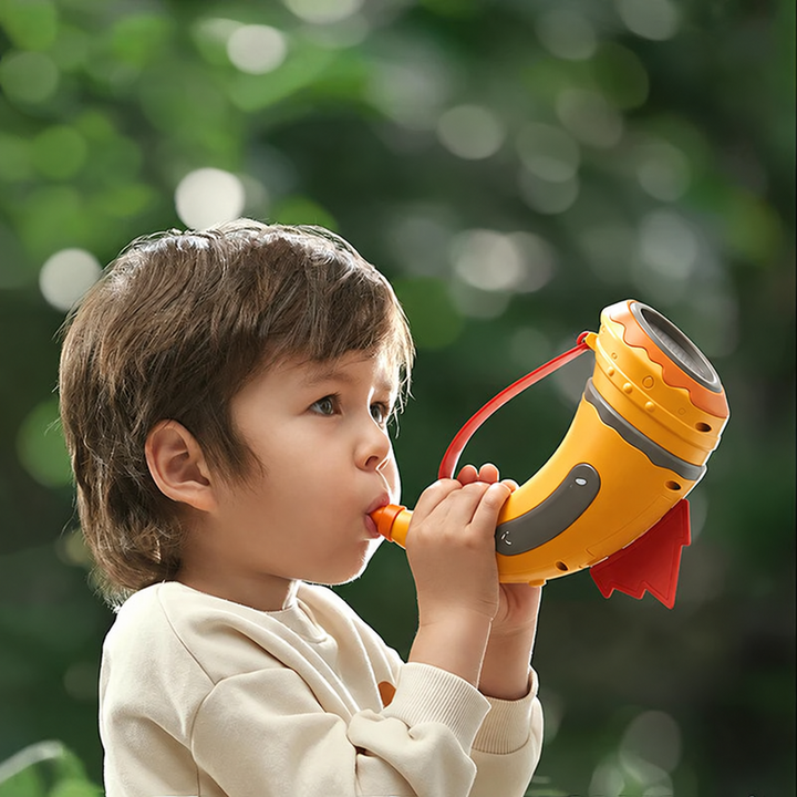 Child blowing into an orange toy horn outdoors