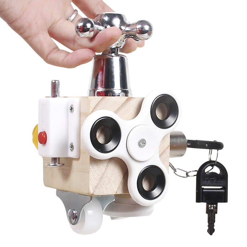 Hand exploring a wooden sensory cube with a faucet-style handle, white spinner, and keyed lock