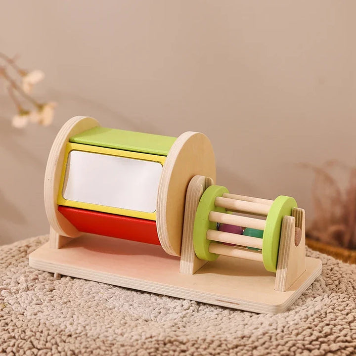 Wooden activity drum with white, green, and red panels and a smaller rattle on the right