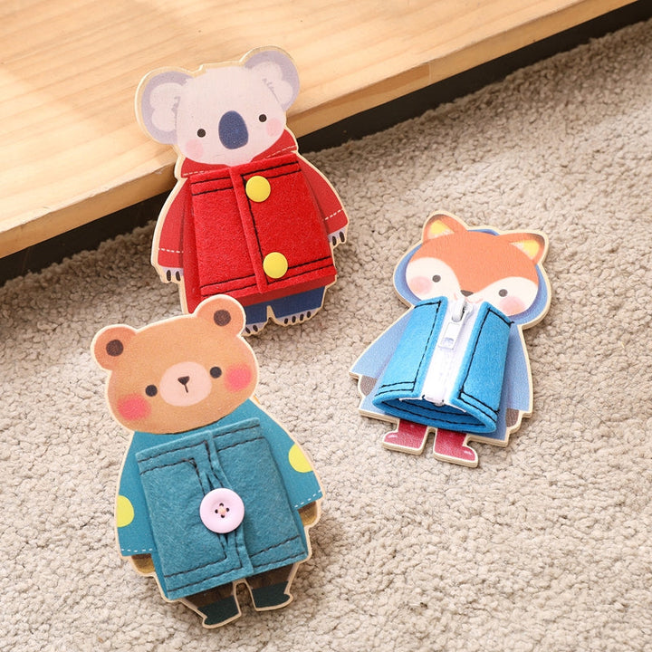 Koala, bear, and fox wooden dressing toys with red, teal, and blue fabric coats on a rug