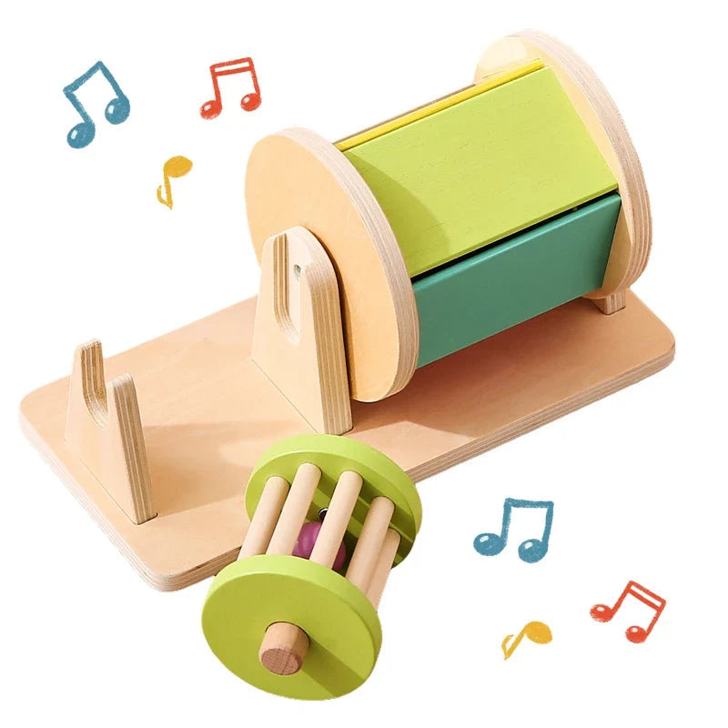 Wooden spinning drum with green panels and a removable cage-style rattle beside its base