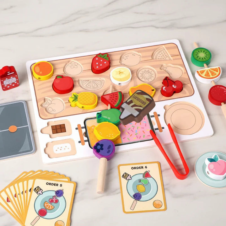 Wooden fruit sorting board with colorful fruit pieces, red tongs, skewers and order cards
