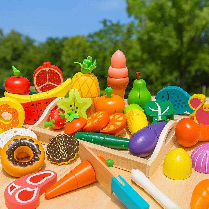 Colorful wooden play food with fruit, vegetables, sweets, and toy knives arranged outdoors