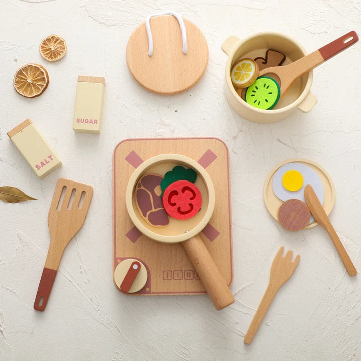 Wooden play kitchen with a stovetop, pot, pan, utensils, and colorful pretend food arranged overhead