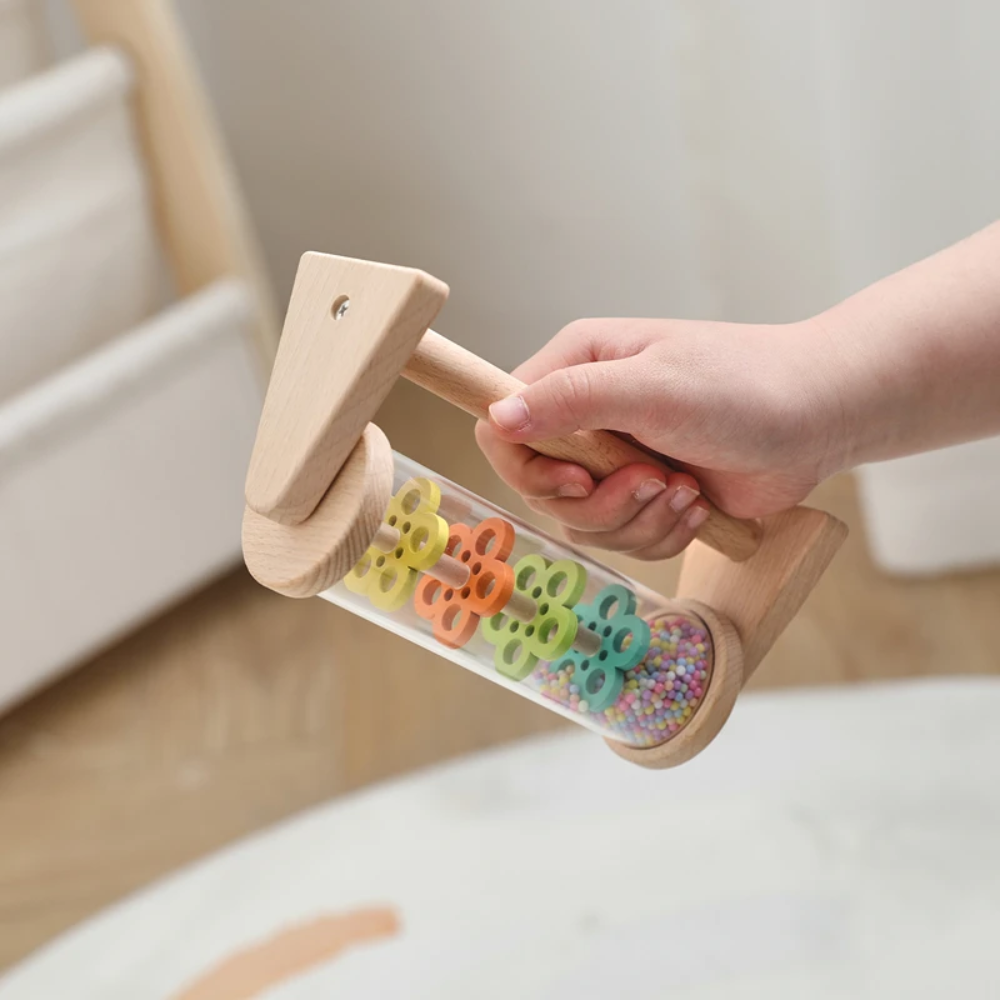 Hand holding the wooden rain sound toy by its frame.