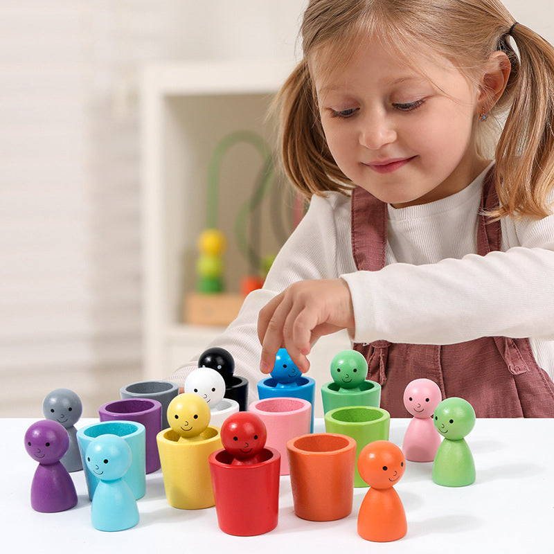 Child playing with wooden color-matching cups and smiling figures at a table