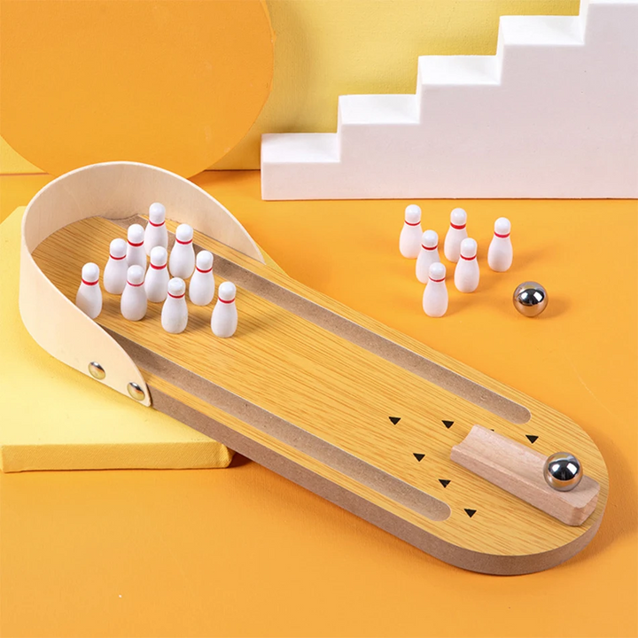 Wooden tabletop bowling lane with white-and-red pins and metal balls on a yellow surface