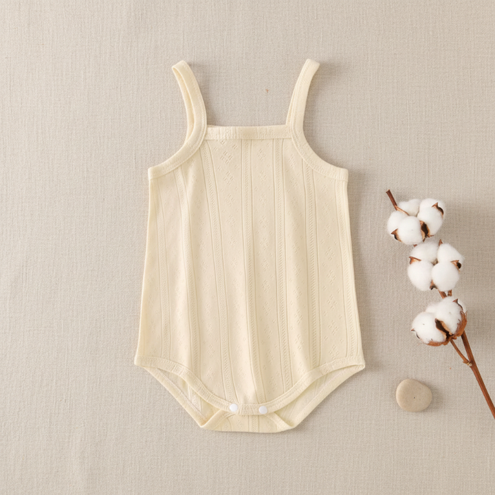 Pale yellow cotton baby bodysuit with thin straps beside cotton stems