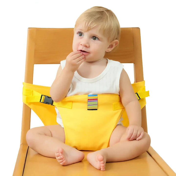 Child wearing a yellow baby chair harness while seated on a wooden dining chair.