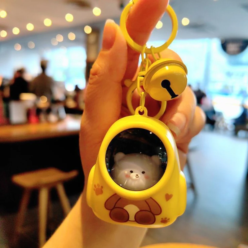 Yellow capsule-style astronaut charm with an animal face, matching key ring, and bell