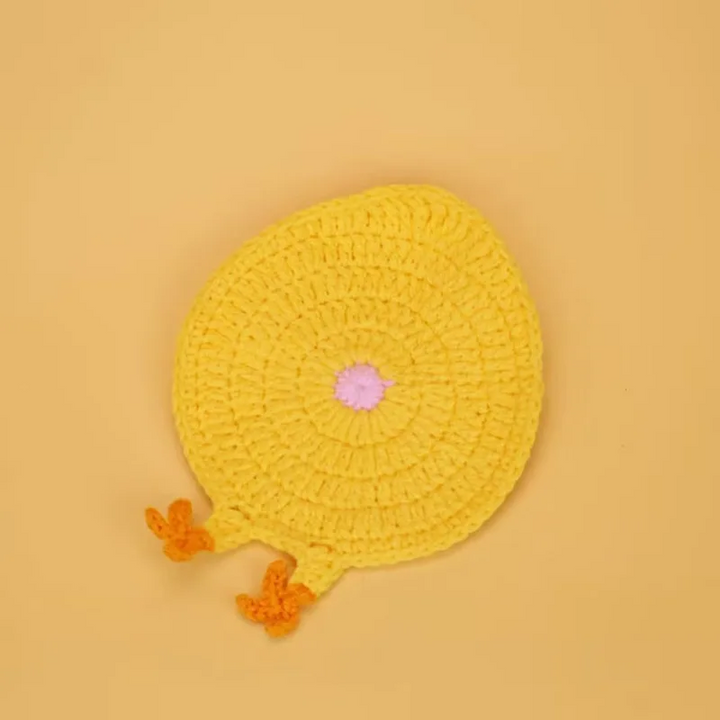 Yellow crocheted chick coaster with orange feet and a small pink center detail