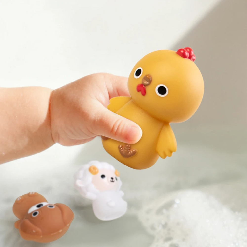 Hand squeezing a yellow chick figure above water with dog and sheep figures nearby