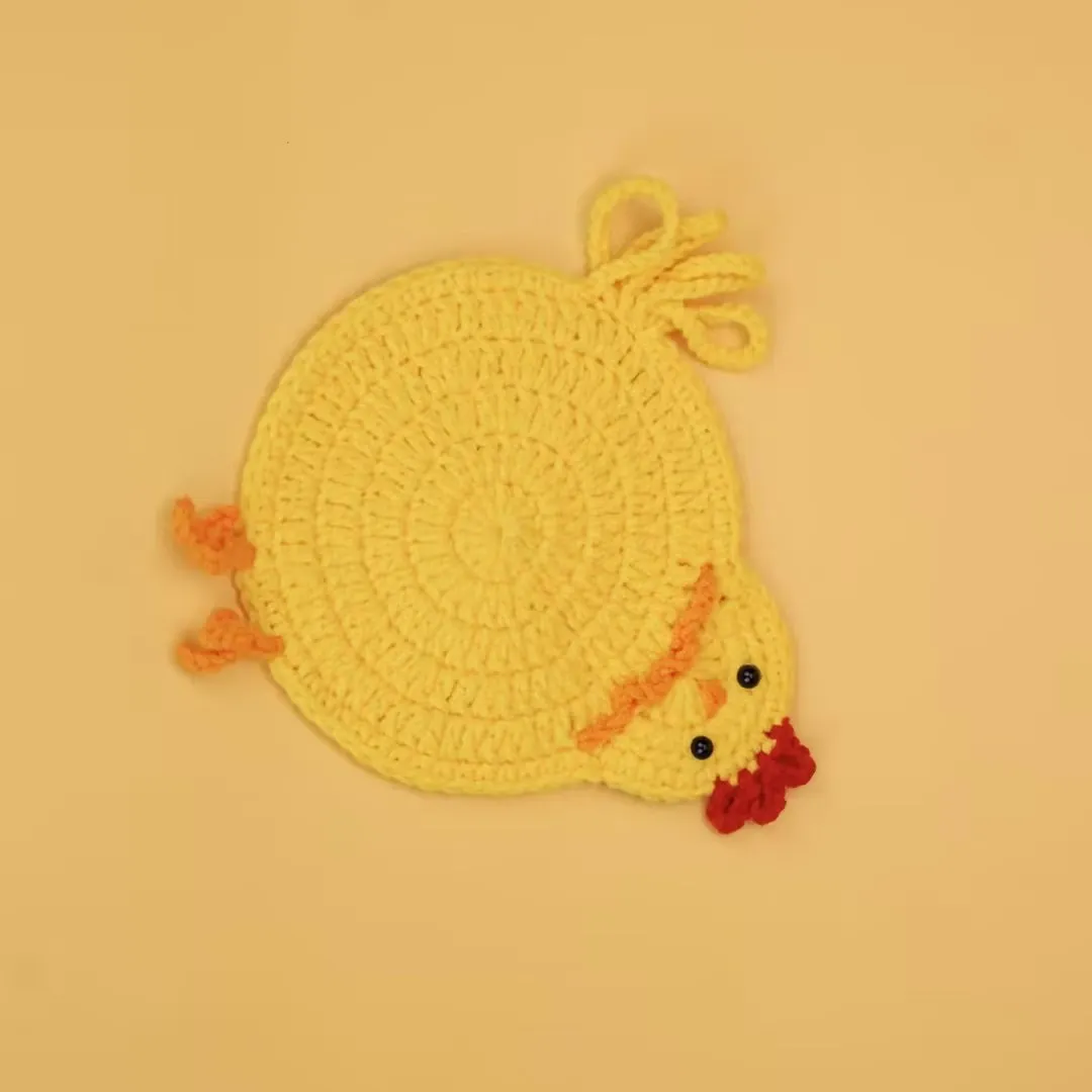 Yellow crocheted chicken coaster with a small head, red comb, and orange feet