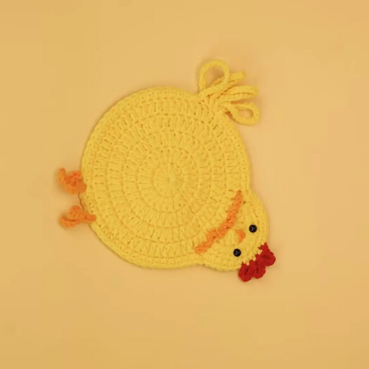 Yellow crocheted chicken coaster with a small head, red comb, and orange feet