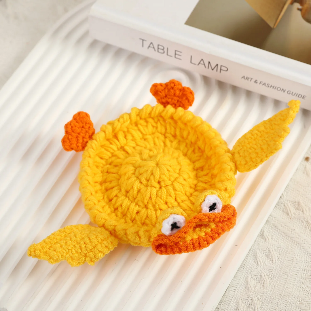 Yellow crocheted duck coaster with an orange bill, small feet, and outstretched wings