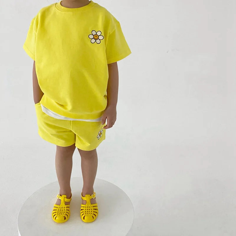 Child wearing a yellow daisy T-shirt and matching shorts with yellow sandals