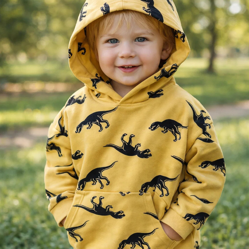 Child wearing a yellow dinosaur hoodie outdoors with the hood up and hands in the front pocket